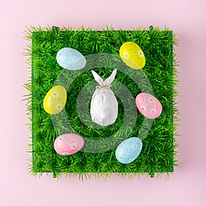 Creative composition with egg wrapped in a paper in the shape of a bunny with colorful Easter eggs. Easter minimal background.