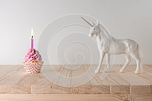 Creative composition with glitter unicorn and pink cupcake on wooden table. Minimal holiday concept