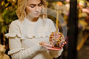 Creative composition in golden pot of Christmas balls and golden candle in hands of blonde