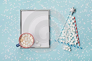 Creative composition with hot cocoa or chocolate, silver frame and fir tree made of marshmallow on winter desk. Christmas mockup.