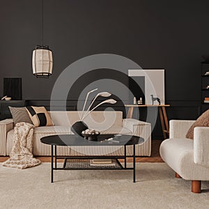 Creative composition of living room interior with modular beige sofa, black coffee table, armchair, rug, black wall with stucco,