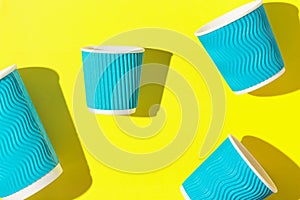Creative composition made of blue paper cups of coffee or tea to go on bright yellow background. Eco friendly concept. Flat lay.