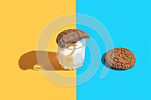 Creative composition made of brown american cookies and a glass of milk on blue and yellow background. Minimal style. Bakery and