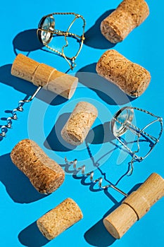 Creative composition made of champagne and wine bottle corks, corkscrews and metal wire muselet on blue sunlit background with