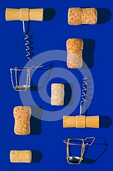 Creative composition made of champagne and wine bottle corks, corkscrews and metal wire muselet on blue sunlit background with