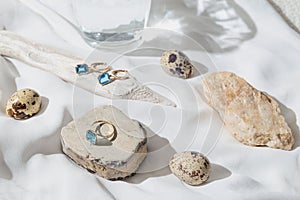 Creative composition made of elegant jewellery set of golden ring and earrings with blue topaz on white background with stones,