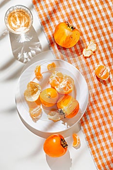 Creative composition made of fresh orange tangerin, persimmon fruits and a glass of drink on white background with palm tree leaf
