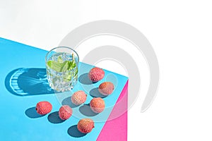 Creative composition made of glass with lemonad and lychee fruits on colorful background. Summer refreshment concept