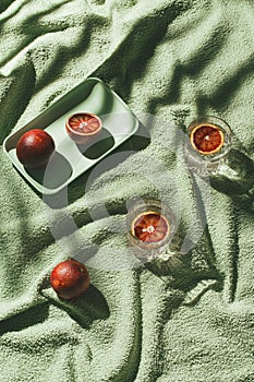 Creative composition made of half bloody red orange on a tray and two glasses with cocktail on green beach towel as a background