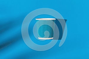 Creative composition made of paper cup of coffee or tea to go on bright blue background with sunlit and shadow. Eco friendly