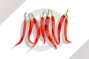 Creative composition made of red chilli peppers on white sunlit background with shadow. Healthy food ingredient concept. Flat lay