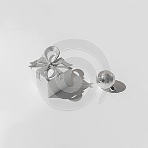Creative composition made of silver present box and decorative bauble on white background with shadows. Christmas and new year