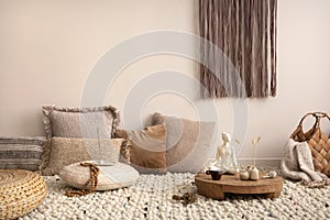 Creative composition of meditation living room interior with beige carpet, pillows, macrame and personal accessories. Home decor.