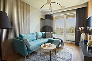 Creative composition of modern living room interior in small apartment. Eucalyptus sofa, designed chandelier, coffee table.