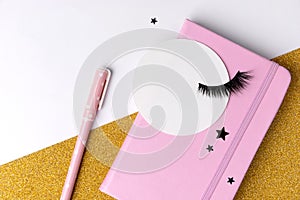 Creative composition with notepad and eyelashes on pink golden glitter background