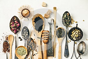 Creative composition with Various kinds of dry tea, silver and bamboo spoons and sugar on white wintage canvas background