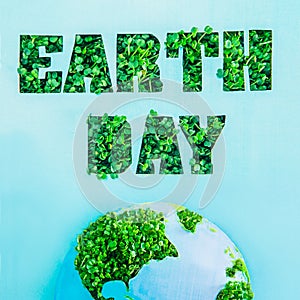 Creative concept with outline lettering Earth Day in green fresh grass sprouts and part of planet model on blue background. Save p