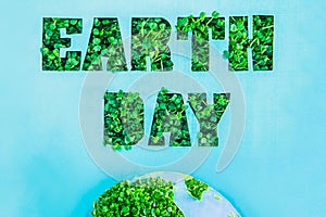 Creative concept with outline lettering Earth Day in green fresh grass sprouts and part of planet model on blue background. Save p