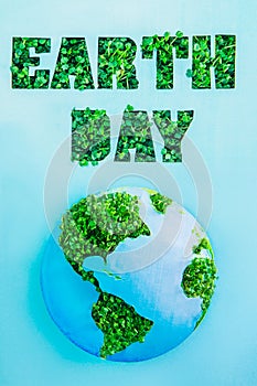 Creative concept with outline lettering Earth Day in green fresh grass sprouts and planet model on blue background. Save planet, n