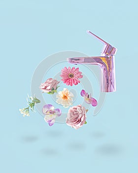 Creative concept of pastel purple faucet from which fresh pink flowers drip. Pastel blue background