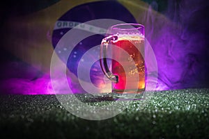 Creative concept. Pint of fresh beer on grass with blurred flag of Brazil on background or Glass of lager beer ready for drink. Co