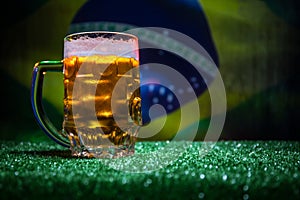 Creative concept. Pint of fresh beer on grass with blurred flag of Brazil on background or Glass of lager beer ready for drink. Co