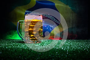 Creative concept. Pint of fresh beer on grass with blurred flag of Brazil on background or Glass of lager beer ready for drink. Co