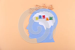 Creative concept. Top view on paper man head with word DREAM inside and crown on it. Light beige background, flatly, copy space