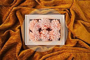 Creative concept of white wood frame with pink spring flowers against golden yellow fabric cloth wave background. Minimal design