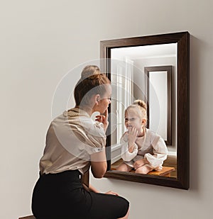 Creative conceptual collage. Young woman looking in mirror and seeing her little self. Back to childhood memories