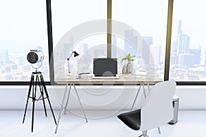 Creative designer desktop with empty laptop computer in modern interior with camera, window and bright city view.