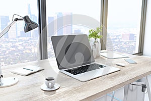Creative designer desktop with empty laptop computer in modern interior with window and bright city view. Mock up
