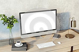 Creative designer desktop with empty white computer monitor, lamp, supplies and other items. Concrete wall background. Mock up, 3D