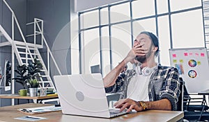 Creative designer yawn while working hard and boring with laptop at modern office.workplace lifesyle concept