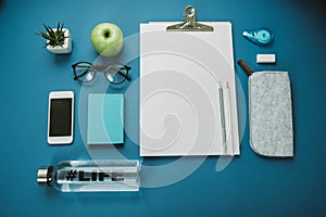 Creative Desktop: pencils, water, apple, phone, glasses, headphones on a blue background. Top view, flat layCreative Desktop: pen