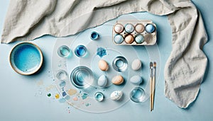 Creative Easter background with eggs, paint, brushes, egg carton and linen cloth. Flat lay on light blue background. Created with