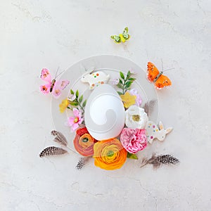 Creative Easter concept made of white egg, bunny, butterfly and spring flowers around on vintage background. Flat lay