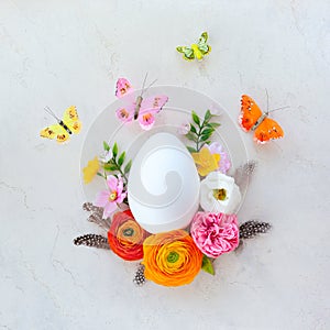 Creative Easter concept made of white egg, butterfly and spring flowers around on vintage background. Flat lay