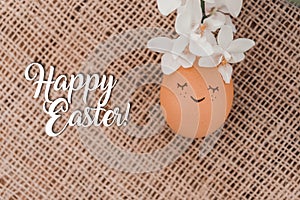 Creative easter egg in floral wreath, cute face and sleepy eyes on sackcloth background. Happy Easter concept