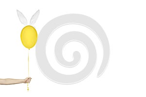 Creative easter minimal concept. Hand holding a yellow balloon in bunny ears isolated on white. Monochrome banner with