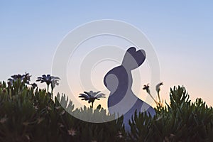 Creative easter photo of silhouette paper rabbit in the chamomile flowers and green grass on the sunset sky background.