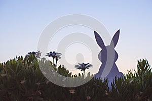 Creative easter photo of silhouette paper rabbit in the chamomile flowers and green grass on the sunset sky background.