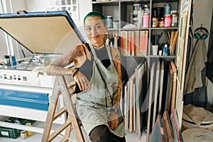 Creative female designer sitting on background of print machine in workshop