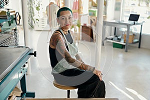 Creative female designer sitting on background of print machine in workshop
