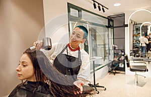 Creative female hairdresser dries hair of client with a hairdryer in beauty salon