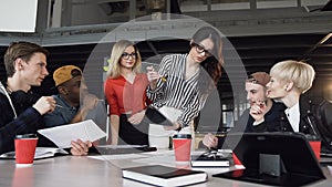 Creative female team leader standing near around table and giving direction to young creative team on meeting at office
