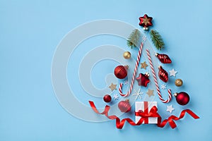 Creative fir tree made of gift box, Christmas tree ornaments and holiday decorations on blue background top view. Flat lay