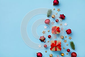 Creative fir tree made of gift box, Christmas tree ornaments and holiday decorations on blue background top view. Flat lay