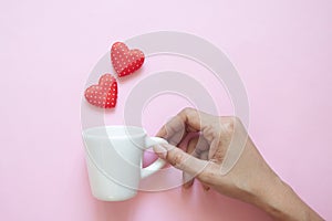 Creative flat lay, woman hand holding white cup with polka dots red hearts on pink background