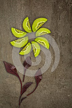 Creative flower made of Kiwis with beetroot leaves cut from below lit on a stone background Food concept